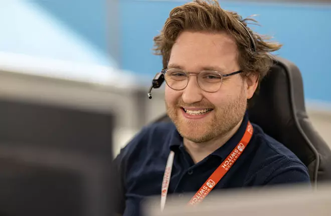 Man smiling behind computer wearing glassess and headset