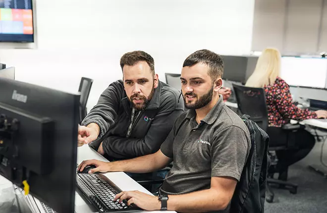 Two men in grey branded polo shirts looking at computer